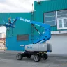 Blue Genie 60 ft. 4WD articulating boom lift with boom extended and worker on platform outside of a building
