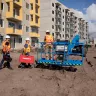 Blue Genie 85-86 ft. 4WD telescopic boom lift with boom lowered and workers stepping onto the platform outside of a construction site
