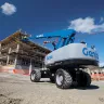 Blue Genie 80 ft. 4WD telescopic boom lift fully extended with a worker on the platform at a construction site