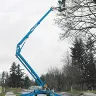 Blue Genie 46-50 ft. 4WD towable boom lift extended with a worker on the platform trimming a tree