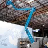 Nacelle élévatrice articulaire électrique Genie bleue de 12,2 m déployée utilisée à l’intérieur d’un entrepôt