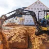 Mini-excavatrice John Deere jaune et noire déchargeant de la terre sur un chantier de construction avec un travailleur dans la cabine