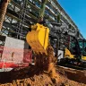 Mini-excavatrice John Deere jaune et noire déchargeant de la terre sur un chantier de construction