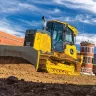 Yellow John Deere small 70 HP low ground pressure bulldozer moving dirt next to a red brick building with a worker in the cab