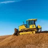 Yellow and black John Deere bulldozer with low ground pressure moving dirt with a worker in the cab
