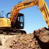 Yellow and black Kobelco zero swing excavator digging dirt at job site