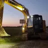 Yellow and black Kobelco zero swing excavator parked on the side of a road at night