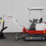 Red Takeuchi mini excavator parked near a wall