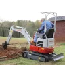 Red Takeuchi mini excavator being used to dig a garden on a lawn