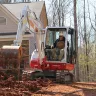 Red and white Takeuchi mini excavator being used to dig dirt next to a house