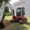 Red and white Takeuchi mini excavator with reduced tail swing parked outside of the Takeuchi plant