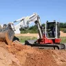 Red and white Takeuchi excavator with zero swing digging in a pile of dirt