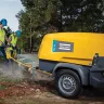 Yellow and gray Atlas Copco compressor powering jackhammers being used by workers to break up concrete