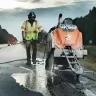 Scie à asphalte autopropulsée Husqvarna orange et grise avec un travailleur marchant à côté sur une route