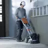 Orange and gray Husqvarna electric single head walk-behind concrete grinder being used by a worker inside a building