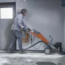 Esmeril para concreto manual eléctrico con cabezal individual Husqvarna naranja y gris usado por un trabajador dentro de un edificio