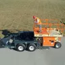 Remorque pour équipement hydraulique au niveau du sol JLG orange sur un chantier avec un travailleur sur la plateforme