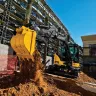 Yellow and black John Deere mini excavator dumping a load of dirt at a construction site