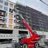 Red and black Magni 11,000-13,200 lb. variable reach forklift fully extended next to a building under construction