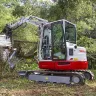 Red and white Takeuchi mini excavator with reduced tail swing being used to demolish an old house
