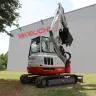Red and white Takeuchi mini excavator with reduced tail swing parked outside of the Takeuchi plant