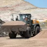 Orange and black Case wheel loader moving a load of rocks using its bucket with a worker in the cab