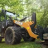 Orange and black Case wheel loader lifting a pallet of cement blocks in a wooded area