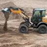 Orange and black Case wheel loader dumping dirt from its bucket with a worker in the cab
