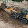 Orange and black Case wheel loader lifting dirt with its bucket on an incline with a worker in the cab