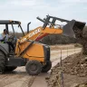 Orange Case wheel loader dumping a load of rocks and dirt from its bucket with a worker in the cab