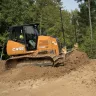 Orange and black Case small bull dozer moving dirt next to a wooded area with a worker in the cab