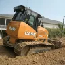 Orange and black Case small bull dozer moving dirt next to a home with a worker in the cab