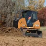 Orange and black Case small bull dozer moving dirt in a wooded area with a worker in the cab