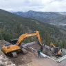 Orange Case excavator with boom extended and digging near a smaller Case excavator on the side of a mountain with workers present
