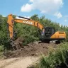 Orange and black Case excavator digging and lifting dirt near some trees
