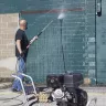 Laveuse à pression Mi-T-M 276 bar argentée et noire utilisée par un travailleur pour nettoyer le mur extérieur en béton d’un bâtiment