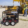 Black and red Mi-T-M 5,000 psi pressure washer being used to wash a piece of heavy machinery