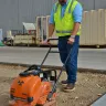 Orange Multiquip Mikasa vibratory plate compactor being used by a worker preparing to pour concrete