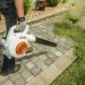 White and orange Stihl hand-held blower blowing grass clippings from a sidewalk
