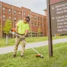 Orange Stihl brush cutter being used to trim grass around a sign in front of a hospital