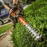 Orange Stihl hedge trimmer with 30 inch blade being used to cut hedges and zoomed in on the cutting blade