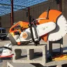 Orange and white Stihl 12 inch concrete cut-off powered off and sitting on top of concrete blocks