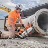 Orange Stihl 14 inch concrete cut-off saw cutting through a concrete pipe