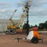 Orange Generac Mobile towable light tower with a 6 kilowatt generator and a vertical mast parked in the dirt at a construction site