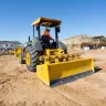 yellow landscape loader on dirt jobsite with blue sky and houses under construction in background