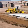 yellow landscape loader on dirt jobsite with houses under construction in background